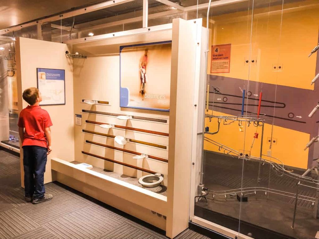 boy looking at a contraption that challenges users to bounce a ping pong ball from one end to the other. 