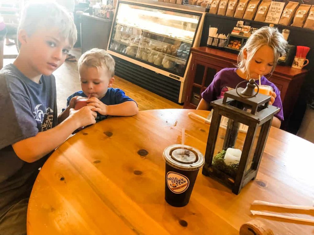 three kids sitting inside of a coffee shop sipping smoothies while a cup of iced coffee sits on the table Cabin Creek Coffee