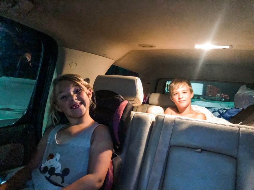Two kids in a dark car with the interior light on with silly smiles on their faces 