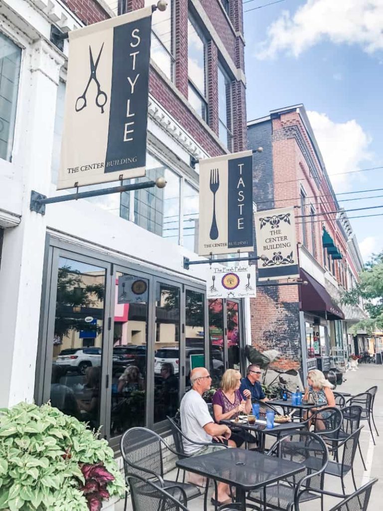 Outdoor restaurant seating with two couples sitting outside enjoying dinner. The banner sign reads Taste, under a sign that says Fresh Palate. 