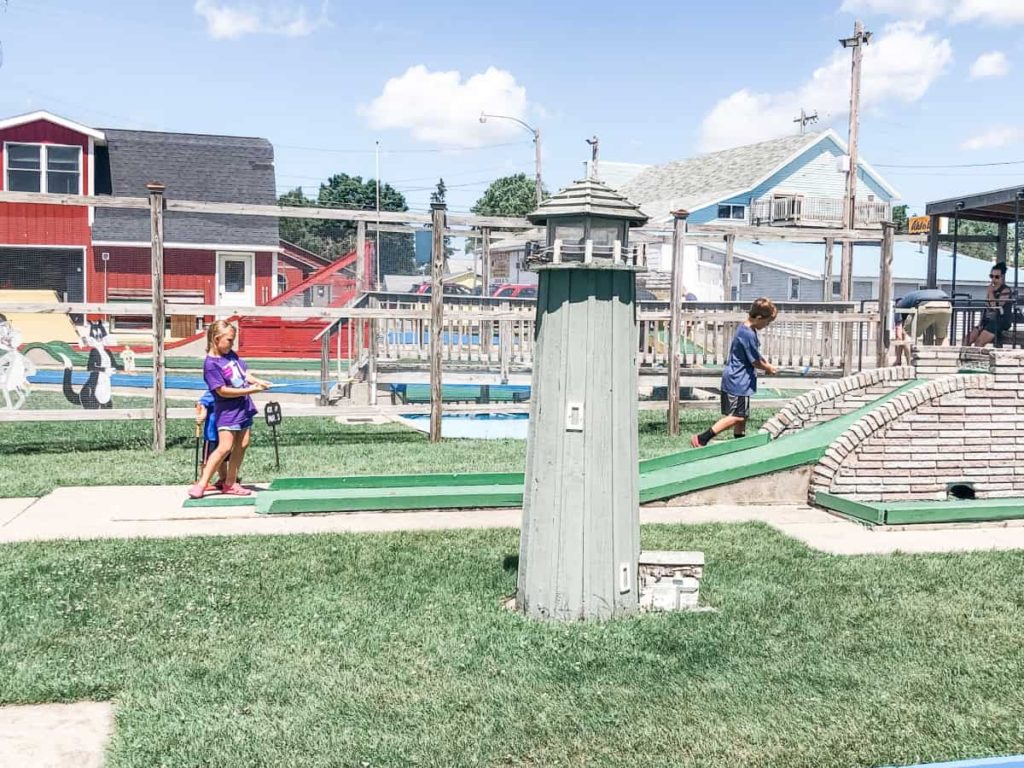 Miniature Golf course. Light house in the forefront, girl golfing a hold in the background, and the red barn further back where you pick up your clubs and balls. 