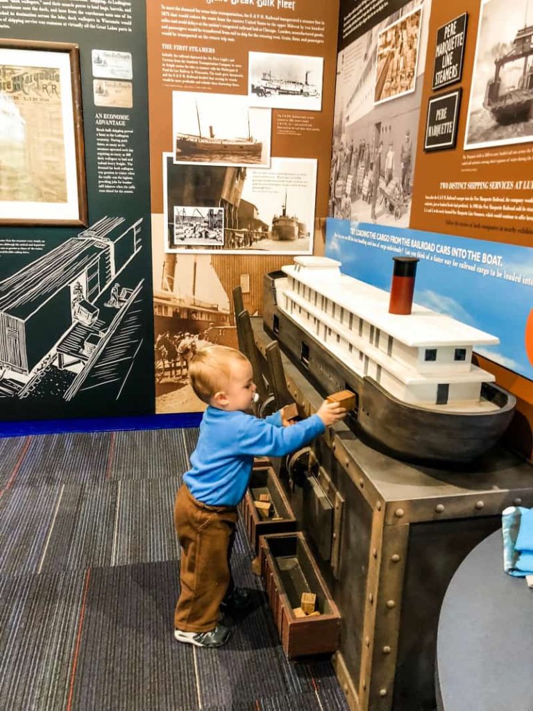 Baby playing with a replica ship. Putting wooden block inside to represent cargo. 