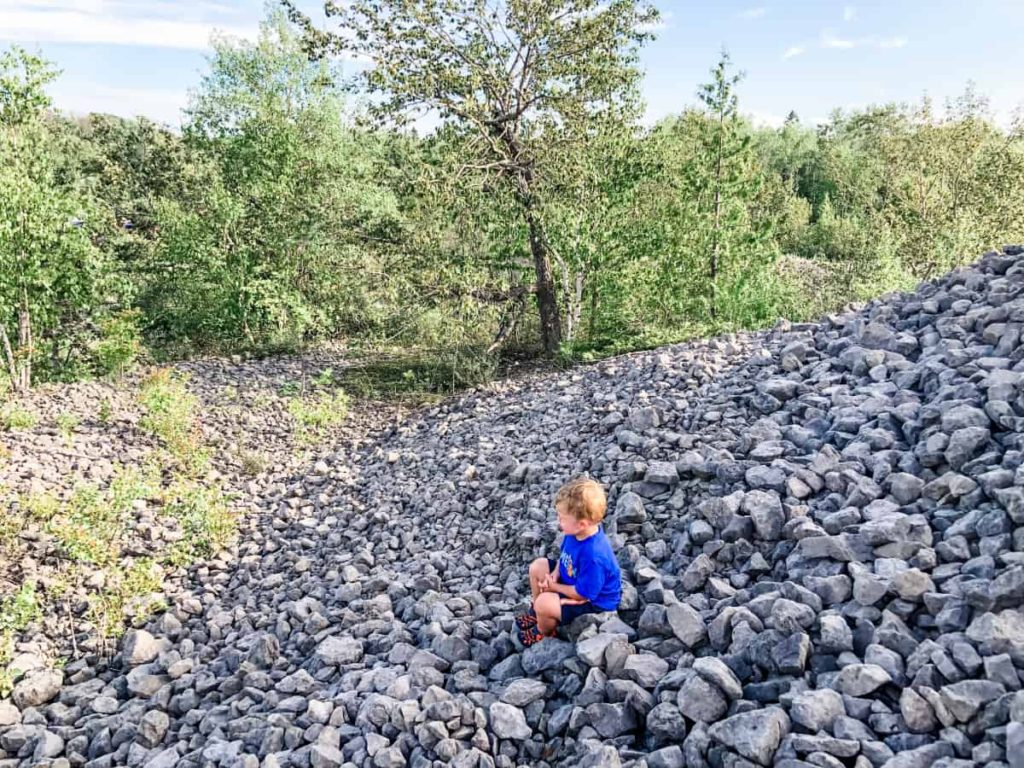 Toddler boy sitting on large hill of rocks crying. Rocks are about 6-12 inches in diameter. 