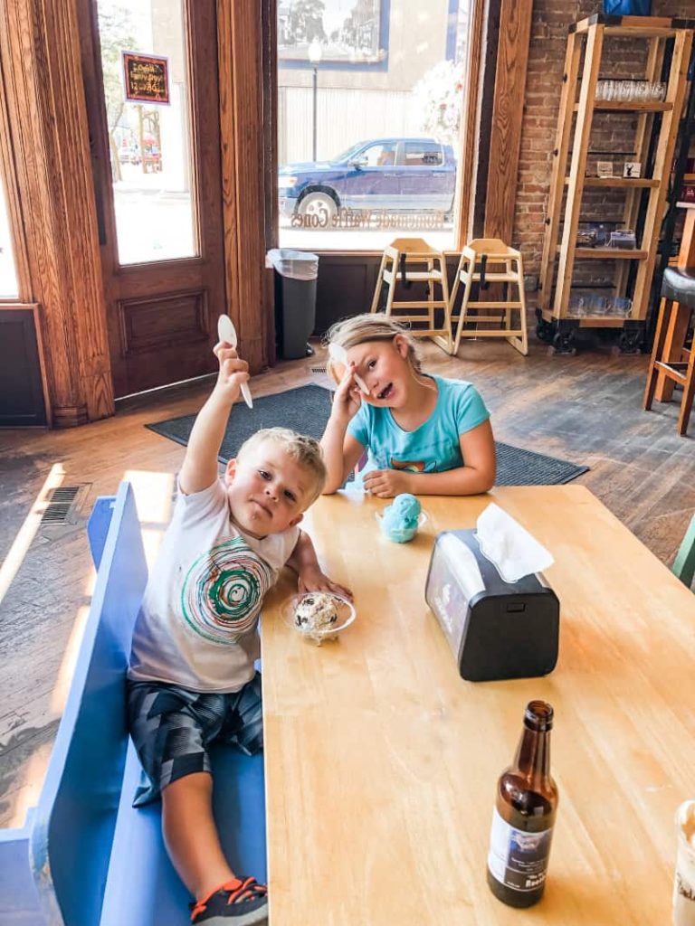 2 kids sitting at a table eating ice cream from plastic clear cups with spoons