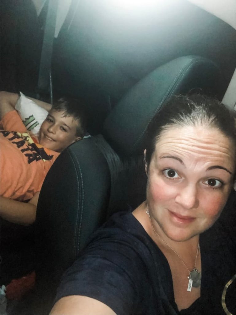 Mother and son, sitting in a car at night, looking amused just before they have to sleep in the car for the night. 