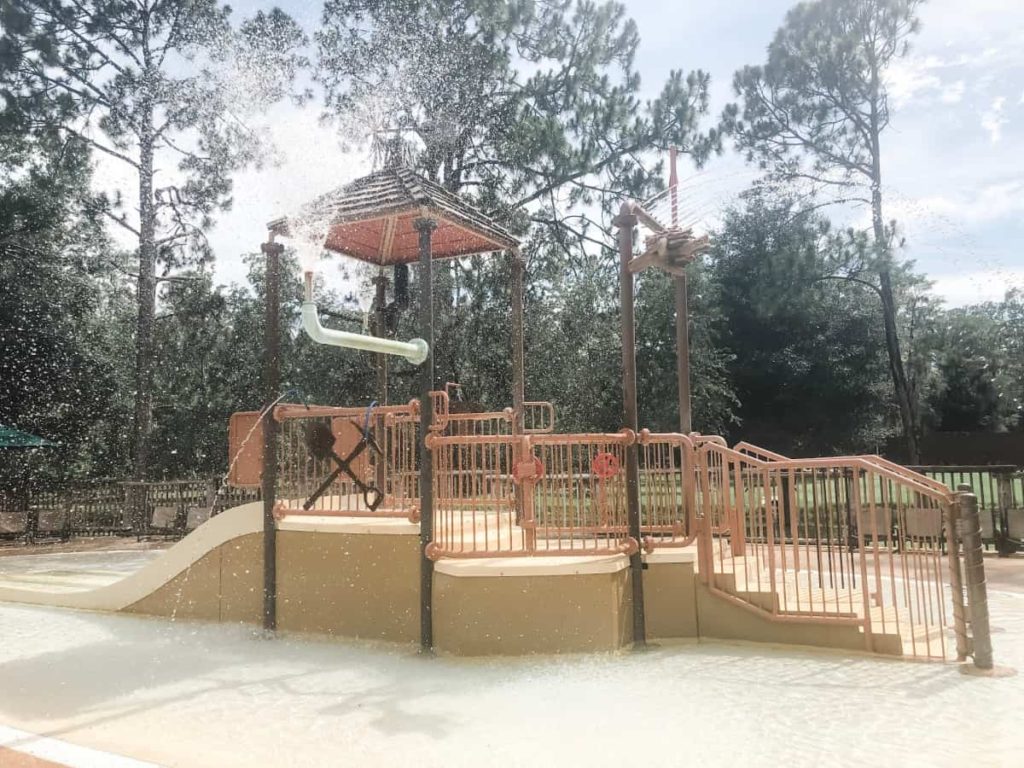 Infant Splash pad area. Water spraying from what is supposed to look like a leaky pipe. Several short stairs lead to a double water slide about 3 feet from the ground. 