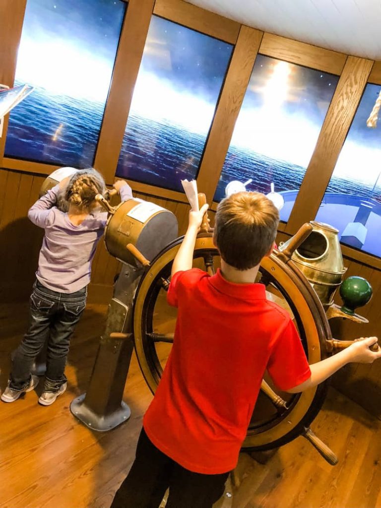 Boy and girl playing with virtual ship. Boy is steering the wheel. Girl is adjusting the thrust.