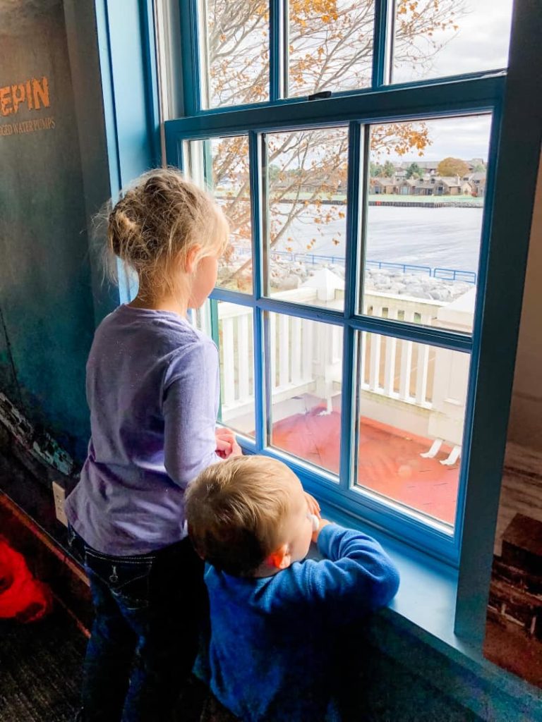 Girl and baby looking out a window searching for ships. 