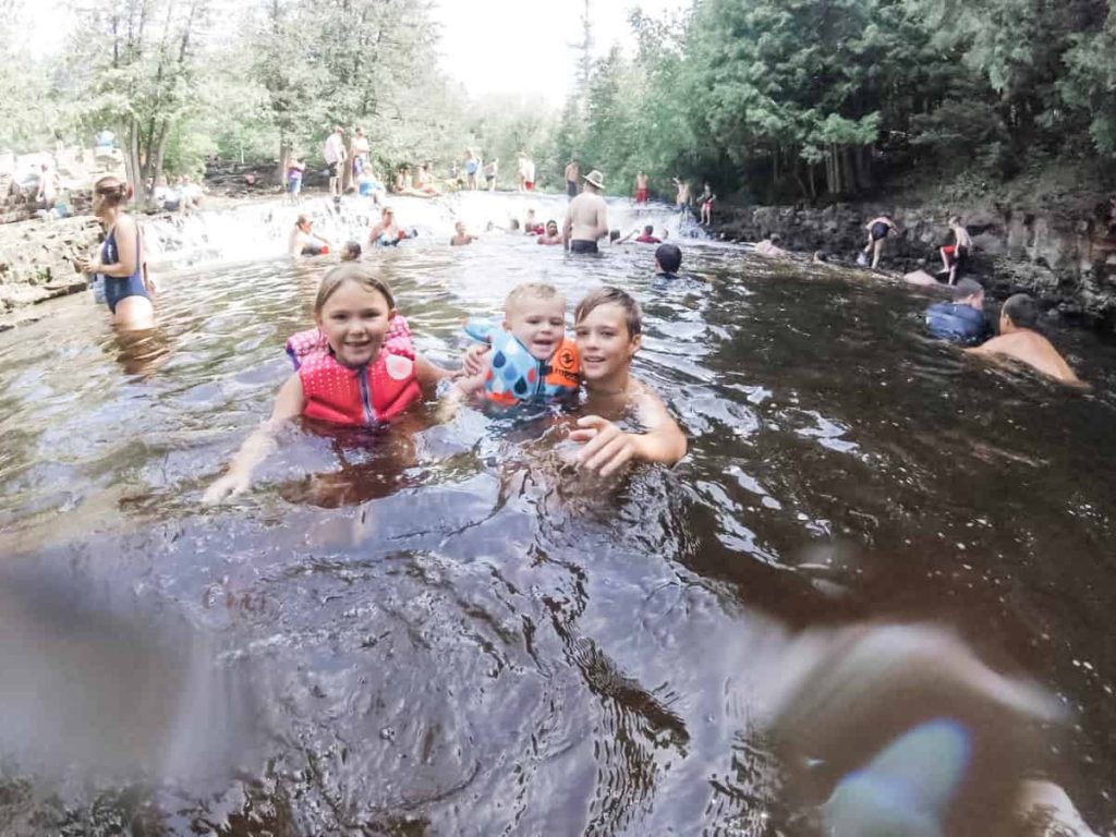 3 kids in the calm water at the bottom of a water fall. 