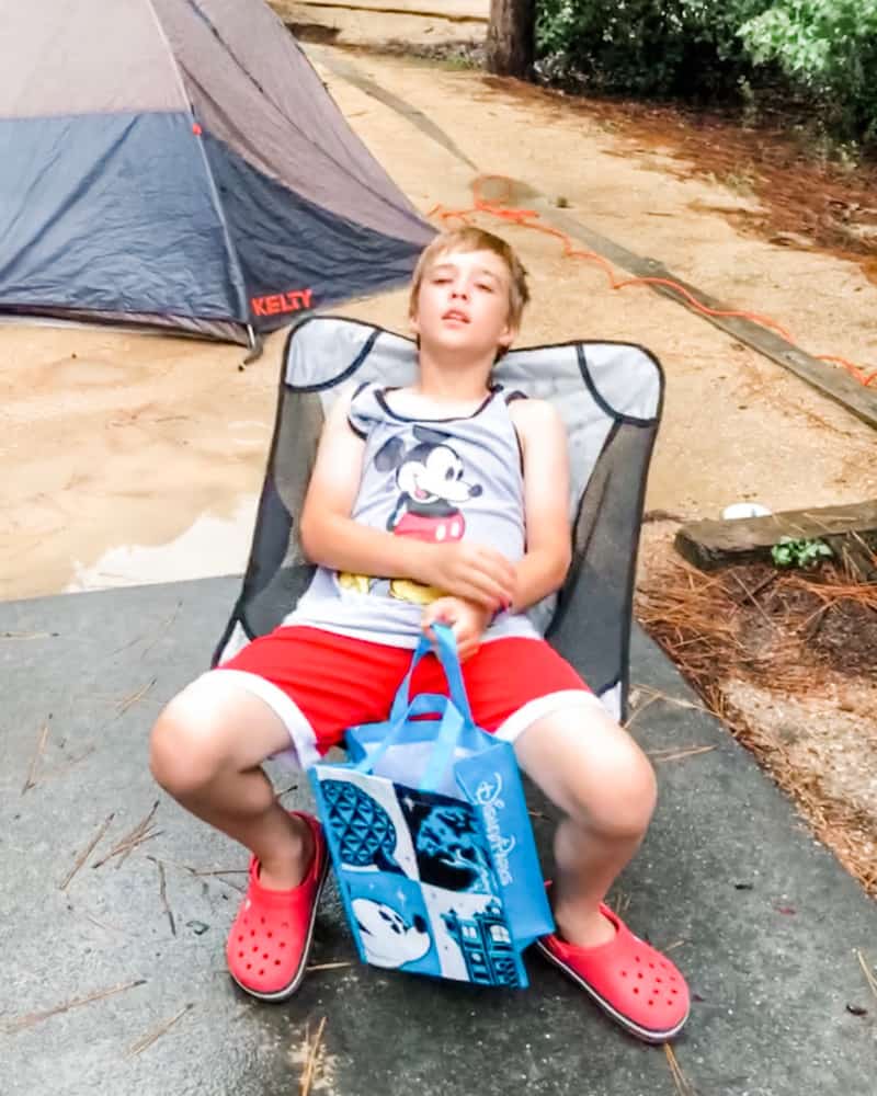 Boy sitting in a camp chair with tent behind him. 