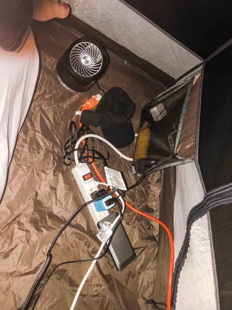a carefully woven set of extension cords, power strip, and many electronics plugged in, including a fan, inside of a tent. 