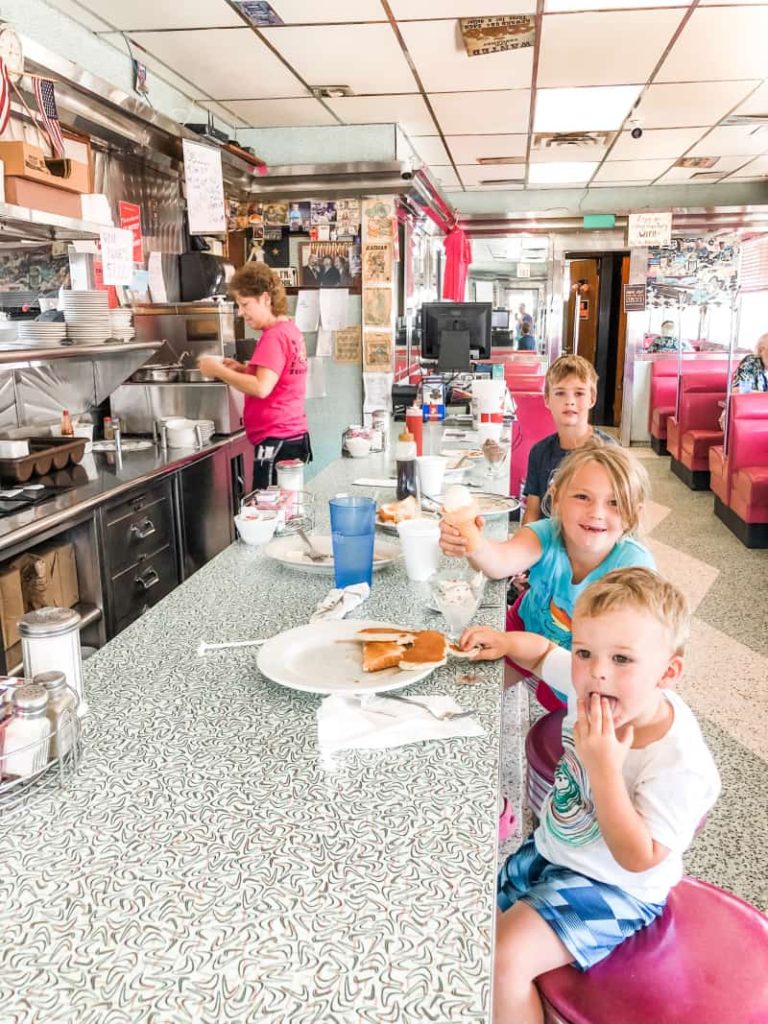 3 kids sitting at the counter of an old fashion diner eating pancakes. 