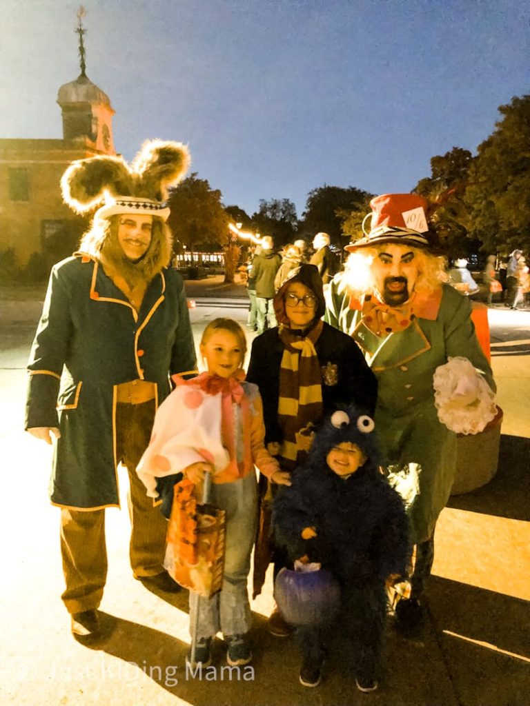 Three kids in halloween costumes standing with actors dressed as characters from alice in wonderland. Mad hatter and rabbit. 