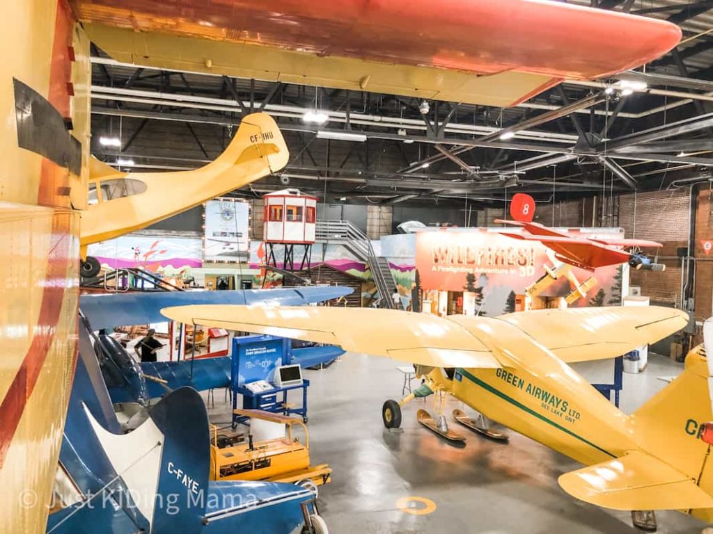 A picture of a lot of museum planes in a plane hanger yellow and blue planes. 