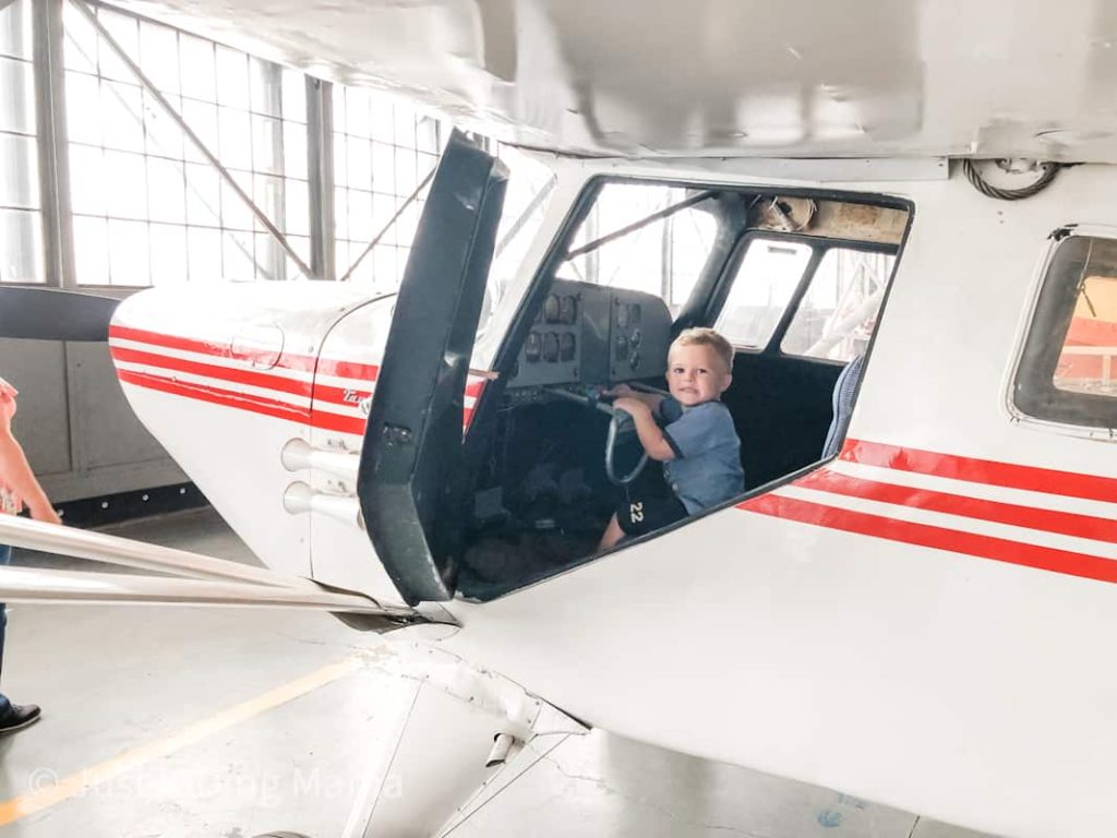 Boy sitting in the cockpit of a white plane with red stripes. 
