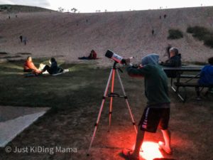 Boy standing in front of a giant sand dune looking through a telescope