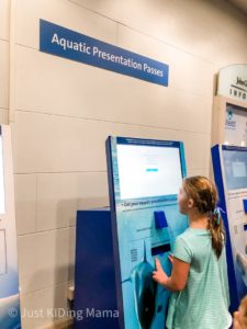 Girl standing at a kisok that will print show tickets sign on the wall says Aquatic Presentation Passes