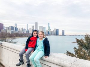 boy and girl sitting on concrete wall with the city of chicago and lake michigan behind them