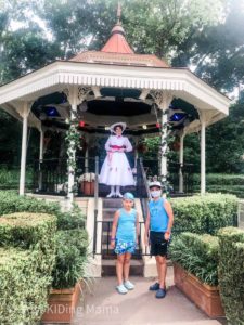 Girl and Boy wearing masks and summer clothes standing in front of Mary Poppins dressed in a white lace dress in a gazebo.