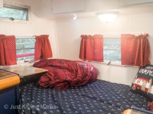 Bed in a camper with navy sheets with anchors small flip down desk on the one side. 