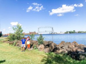 2 boys and a girl standing in a park with an Ariel lift bridge in the background