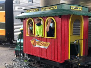 Small pretend train caboose used for a photo booth, 2 boys and a girl inside looking out the windows