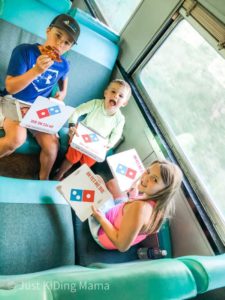 2 boys and a girl sitting on a passenger train holding Domino's Pizza boxes