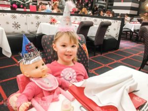 Young girl with birthday hat sitting at restaurant next to a doll also in a birthday hat