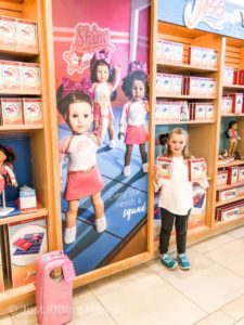 Girl Standing in front of a poster Display of the Girl of the Year at American Girl store