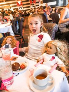 GIrl sitting in a restaurant with 2 dolls at the table 