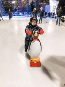 Boy in snow gear and hockey helmet is pushing a plastic penguin on the ice 